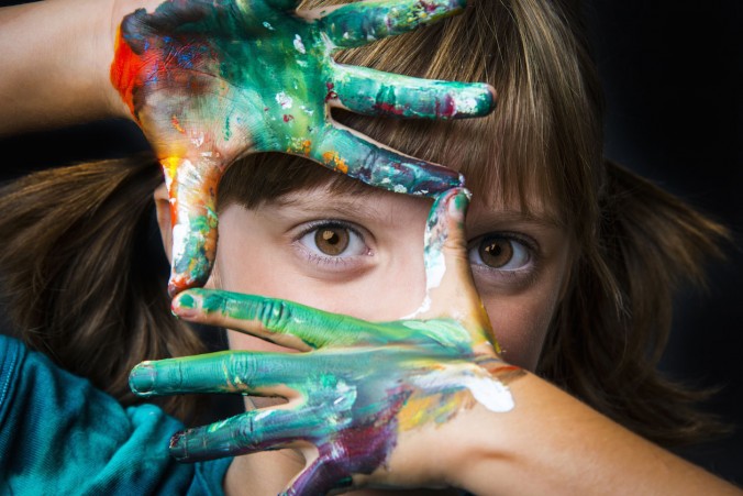 Photo of girl looking through painted hands at viewer.